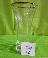 Front view of clear crystal vase with gold rim on top, standing against a green background.