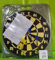 Front view of the dart board set inside clear plastic packaging, showing dart board, 4 darts, and instruction sheet.