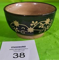 Side view of the ceramic bowl showing the hand painted floral vine motif with a dark green background and dark rim.
