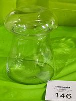 Clear glass candy dish shaped like a mushroom showing the profile and side view, placed on a green background.