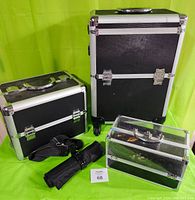 Travel luggage set with black textured cases edged in silver metal, includes one small shelf case, one medium sliding tray case with shoulder strap, one roll-up kit, and one large wheeled base case with pull handle.