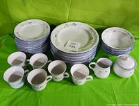Full set of dishes including stacked plates, cups, sugar bowl, and cream pitcher arranged on green cloth background.