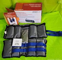 Photo showing adjustable ankle/wrist weights with one missing weight pouch, original box and manual in background.