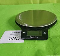 Front angled view of Starfrit digital kitchen scale showing stainless steel platform, display, and buttons on black base with auction lot number.