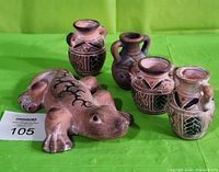 Set of one terra cotta gecko figurine and four terra cotta jugs with Southwestern style painted designs on green backdrop.