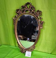 Front view of vintage oval Durwood mirror with ornate cast metal frame against green background.
