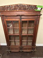 Front full view of antique kitchen cabinet showing glass panel doors, drawers, and carved top detail