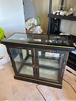 Front view of the black Asian display cabinet with glass top and front display area showing floral gold accents.