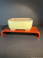 Photo of a rectangular 5 inch bonsai planter in light green glaze on a wooden display stand, showing side perspective