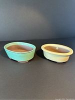 Two ceramic bonsai planters side by side, one green glazed and one beige glazed, showing front and top view