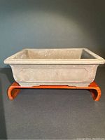 Front angle view of purple terracotta bonsai planter on wooden stand, showing rectangular side panel and textured surface.