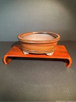 Front angle photo of the brown glazed oval bonsai planter showing figured feet and rim detail, placed on a wooden stand