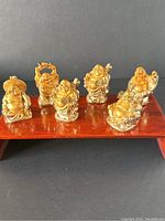 Lot of 6 gold painted resin Buddha figurines on display stand, showing all pieces