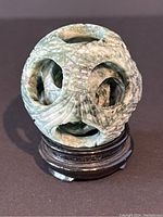 Front view of green jade carved mystery ball on wooden stand showing carved circular cutouts and smaller inner spheres.