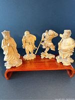 Four vintage Chinese boxwood figurine carvings displayed on a wooden stand
