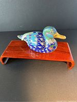 Photo of the cloisonné duck on a wooden stand, showing the left side profile with vibrant blue and green enamel and gold beak.