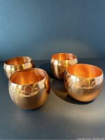 Four solid copper rounded drinking vessels shown from the side and top view. Reflective polished surface with minor wear marks visible.