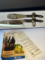 Set of two stainless steel knives with engraved handles in a white display box along with Cutco pamphlets.