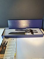 Two cutting knives with serrated blades and ergonomic handles in blue Cutco display box with instruction booklet visible to the side.