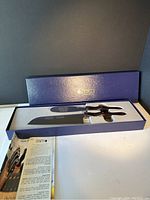 Image of two Cutco knives in original blue display box with foam cutouts, one large butcher knife and one smaller knife visible, along with informational pamphlet.