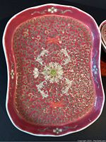 Close-up of tray showing the intricate gold scroll pattern and central floral design in white and green on a deep pink background.