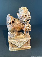 Front and angled view of brown soapstone Foo Dog sculpture on decorated pedestal.