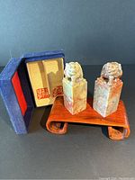 Two hand-carved foo dog stone ink stamps displayed with original box containing paper with red stamp impressions and a wooden stand (stand not included).