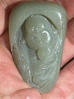 Photo showing jade laughing Buddha carving in hand, highlighting overall size and shape with smooth polished surface and carved details.