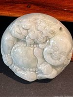 Front of round green jade pendant with carved Happy Buddha holding a large pearl, detailed carving visible, bead necklace and joyful facial expression