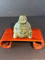 Front view of green jade Buddha figurine seated on wooden stand showing detailed facial features and hand carving.