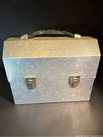 Closed vintage Aladdin aluminum lunch box showing embossed brand and black handle.