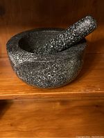 Side view of heavy black granite mortar with pestle inside resting on wooden shelf