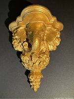 Front view of gold painted small shelf showing elephant head with floral carvings.