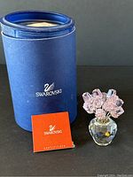 Full view of Swarovski crystal flower bouquet with box and certificate in foreground on black background.