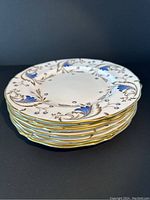 Stack of eight salad plates showing hand painted blue floral and gold gilded rim design.