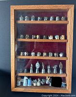Full view of oak display cabinet holding 43 assorted decorative thimbles across five shelves with red velvet backing
