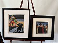 Photo showing both framed artworks on display, one larger with colorful building and dancing couple, the other smaller with social group scene.