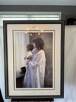 Full view of the framed print showing a mother holding a baby wearing white garments, set in a black frame with white matting.