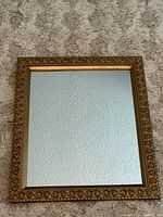 Full frontal view of rectangular mirror with gold gilt frame on carpeted floor.
