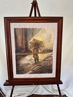 Framed full view of the signed watercolour painting depicting a child with an umbrella on wet pavement