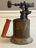 Full side view showing the shape, red handle, valve and nozzle of the antique blow torch.