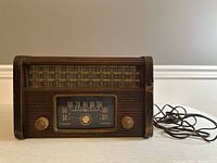 Front view of vintage General Electric radio showing wood casing, metal mesh grille, tuning dial, and power cord.