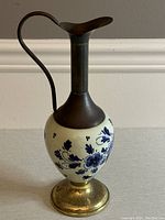 Front view of Delft ewer showing ceramic bulbous body with blue floral pattern and metal neck, spout, handle and base.