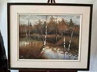 Framed landscape painting with birch trees along water, signed by the artist.