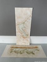 Photo showing two original Inuit art paintings positioned on floor and against wall; one vertically oriented leaping fish painting, one horizontally oriented polar bears painting.