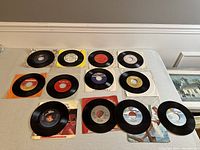 12 vintage 7 inch vinyl records laid out on a table with sleeves, various colors and labels visible