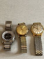 Three vintage watches laid side by side on a fabric surface showing front faces and metal bracelets.
