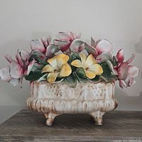 Full view of large vintage porcelain centerpiece with pink, white, and yellow flowers on ornate footed cream base.