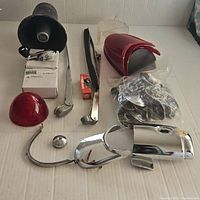 Overall lot of vintage car parts including horn, wiper arms, red mirrors or fins, chrome trim on a white backdrop