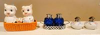 Wide shot of three sets of salt and pepper shakers: pig family in basket, blue glass pair, round ceramic floral pair